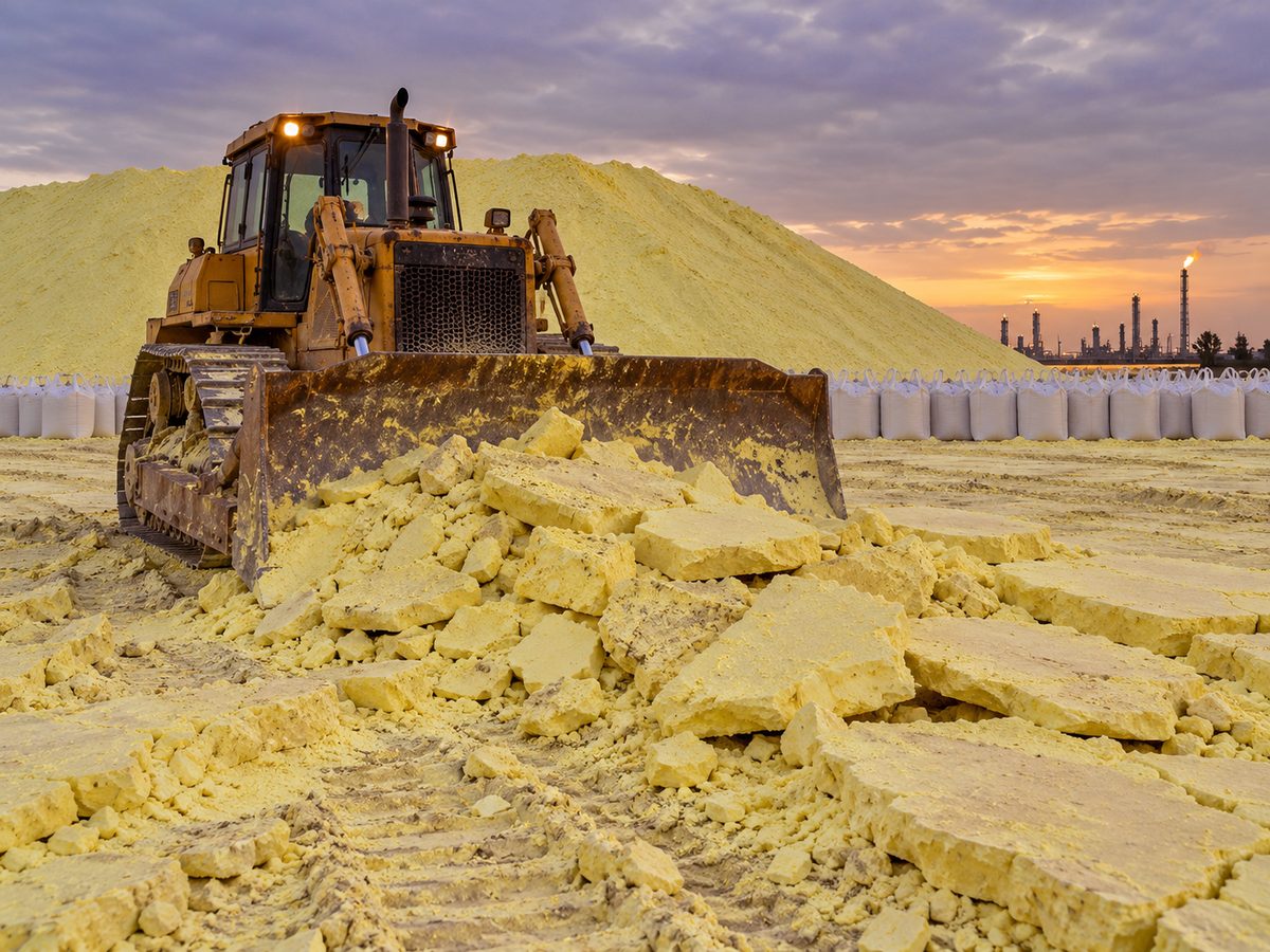 Bulldozer breaking hardened sulfur at a storage yard beside a gas processing plant